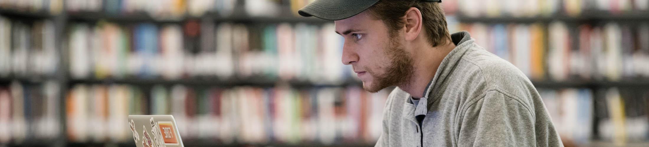 Male student working on laptop in library.